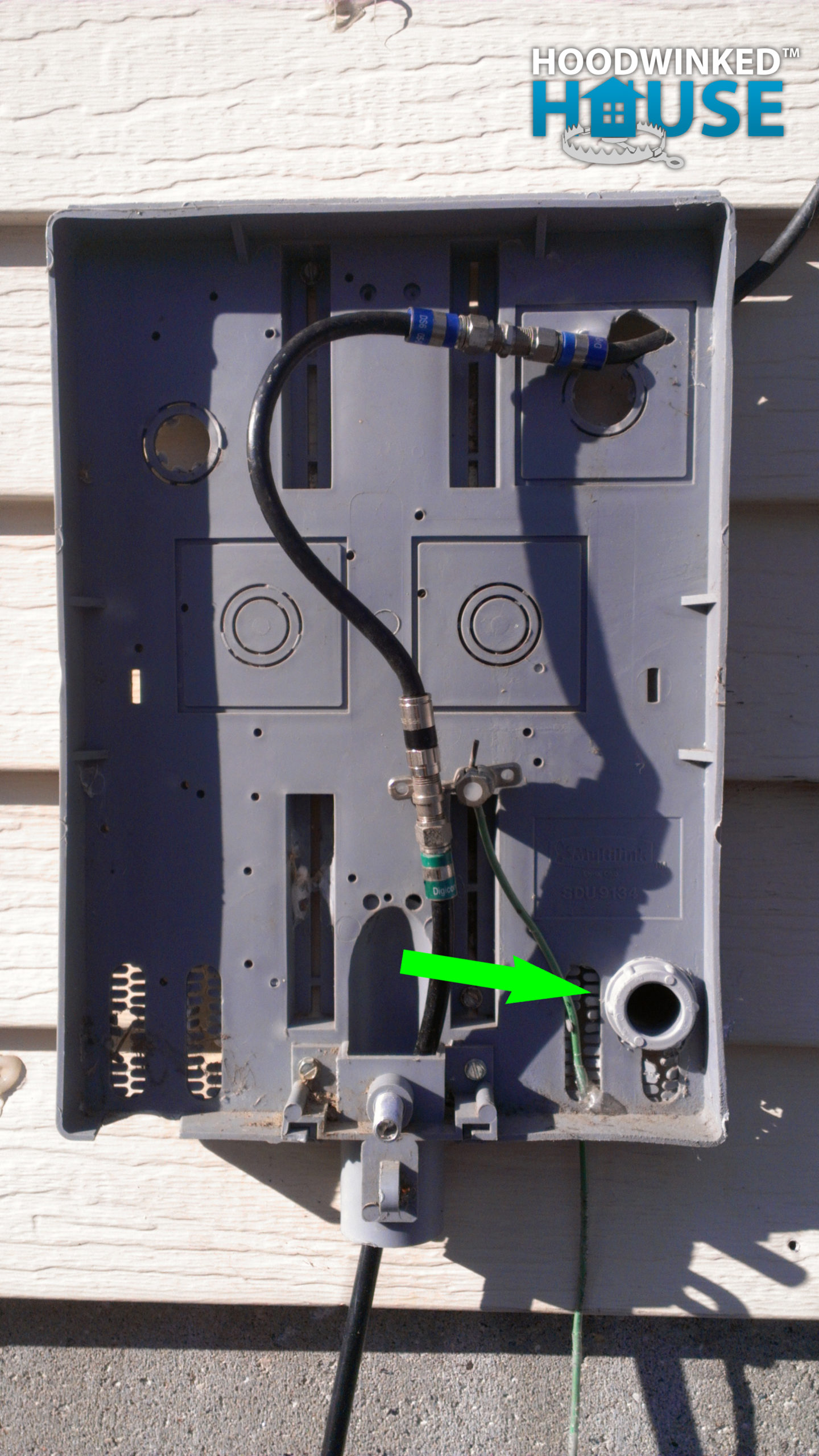 A cable TV service box with a conduit connector exiting the back is mounted to the exterior of a house.