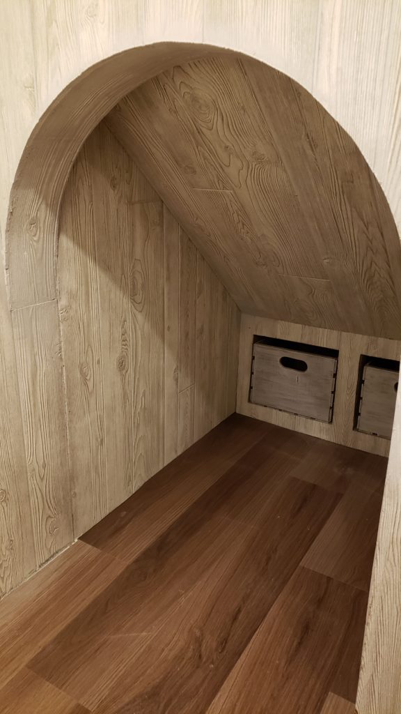 Beneath a staircase, a pair of crates are used as drawers. The underside of the staircase if finished with textured paneling.