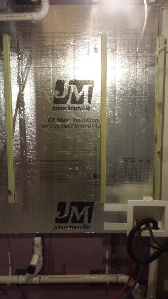 Fire resistant insulation is added to a basement wall around some framing for a pair of electrical service panels.