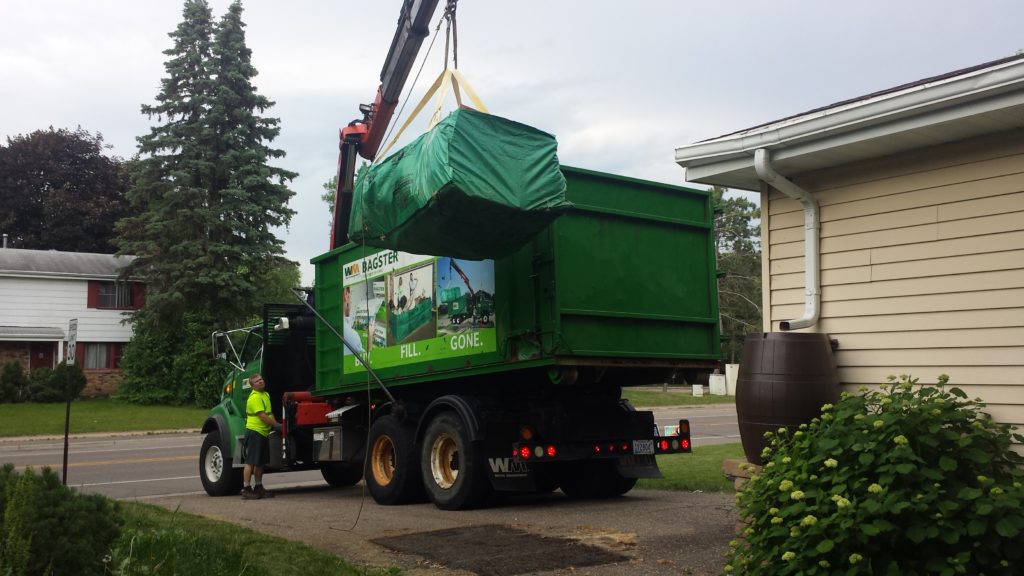 A Waste Management truck hoists a Bagster up to be hauled away.